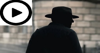 A man in a wide hat walks in the street, in silhouette.