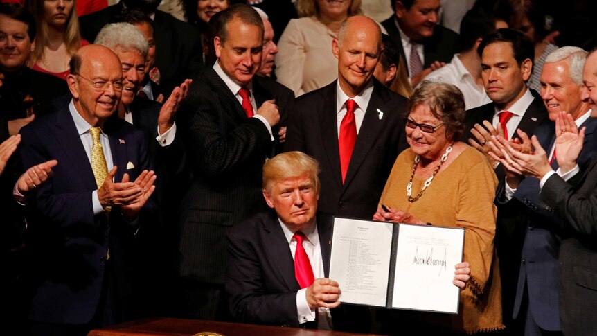 US President Donald Trump, surrounded by congressmen and others,  holds a document he signed after announcing his Cuba policy.