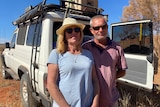 A couple stand in front of a 4WD vehicle in the Central Australian outback.