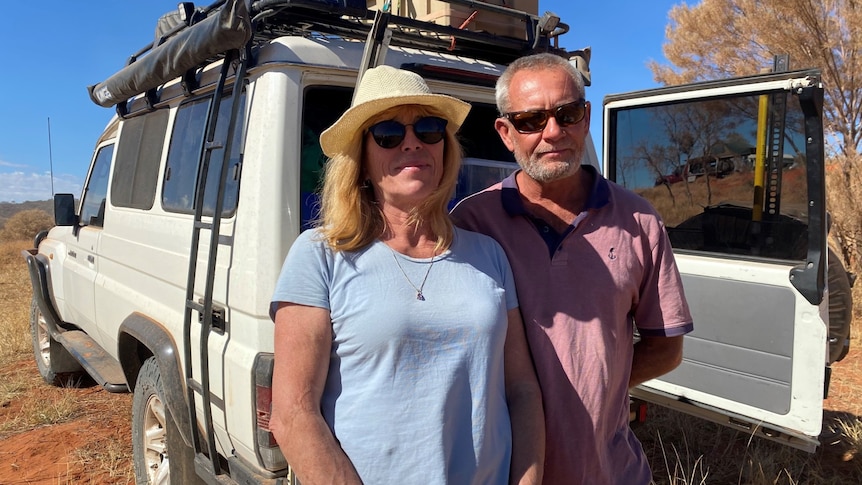A couple stand in front of a 4WD vehicle in the Central Australian outback.