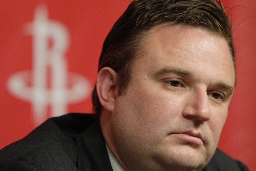 A man looking serious in front of a Houston Rockets background