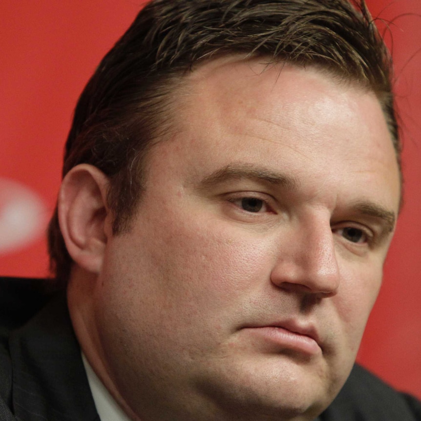 A pensive-looking man sits at a table during a press conference.