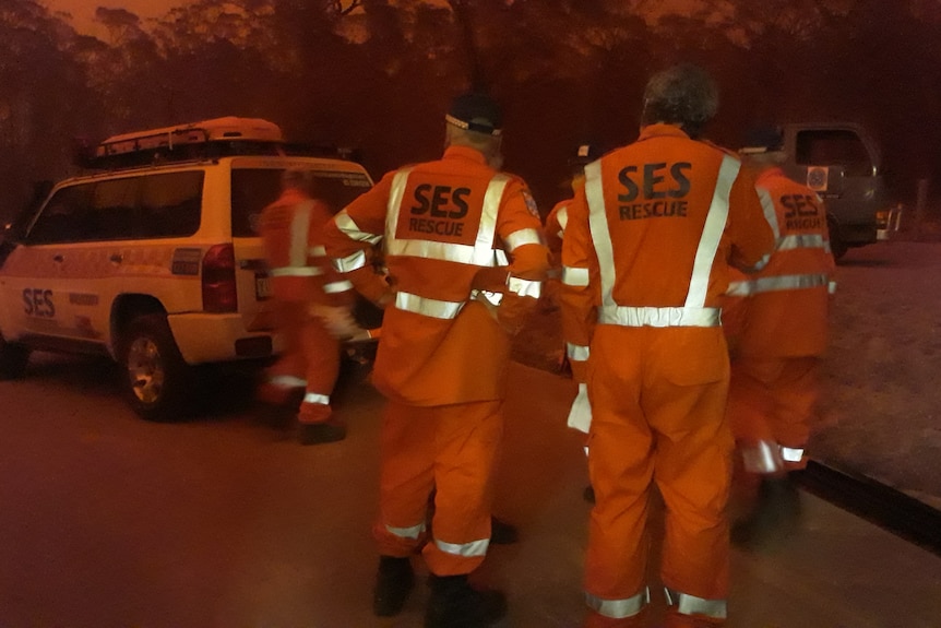 Two men standing near an SES car, everything has a red haze because of the bushfires