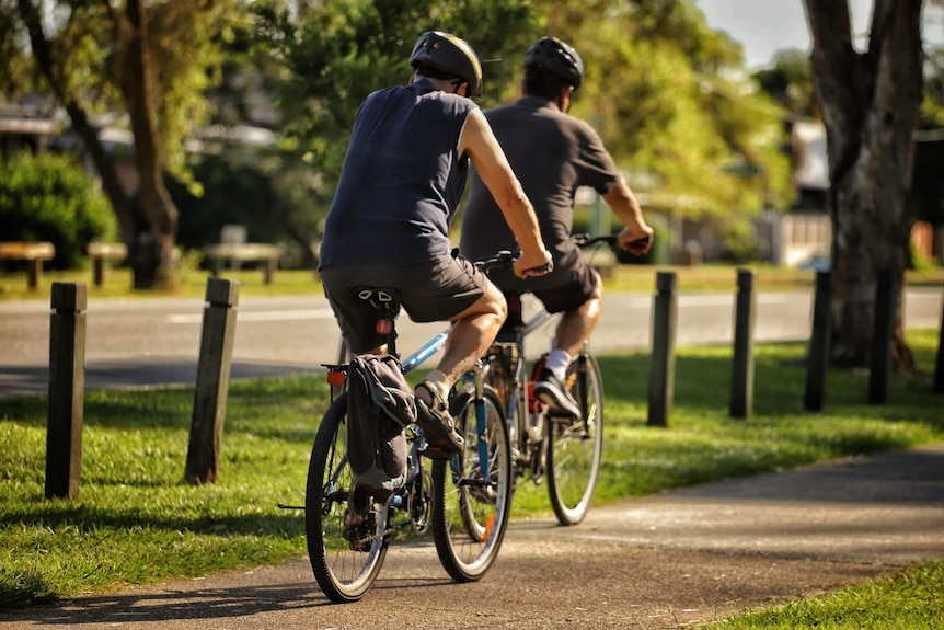 Two men ride bikes along a cement path.