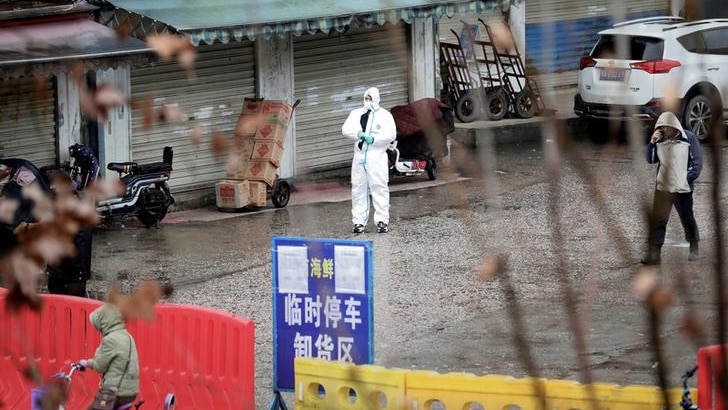 A man in a hazmat suit standing outside a Chinese marketplace