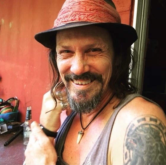 Man in a singlet with a tattoo on his arm, wearing a hat.