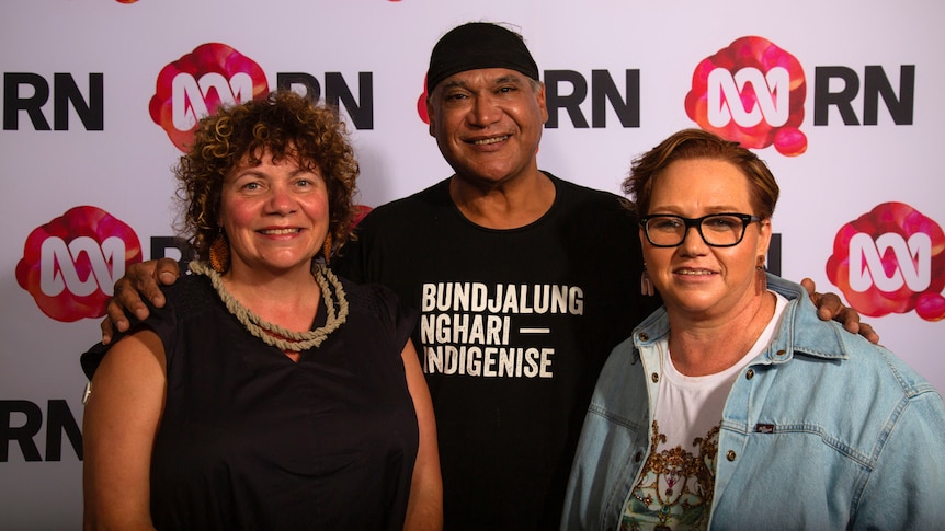 Priscilla Reid-Loynes, Mark Olive and Sharon Winsor stand in front of a Radio National media wall. 