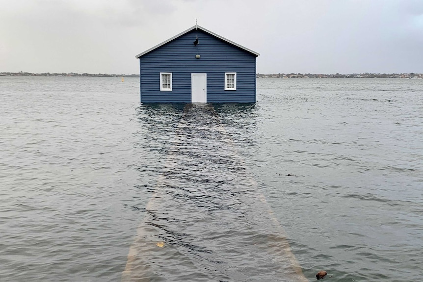 The flooded walkway leading to a blue boathouse in a river.