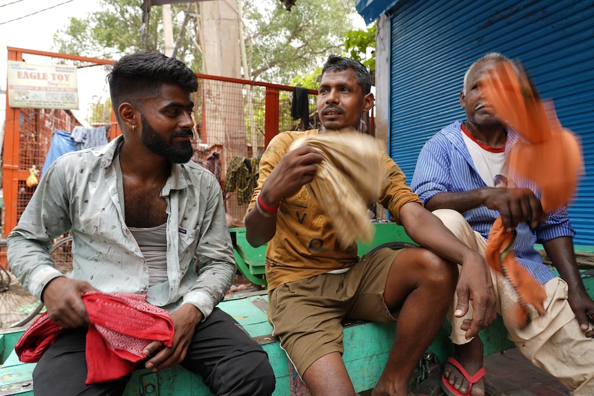 Three Indian men sit in a street waving handkerchiefs around to cool down