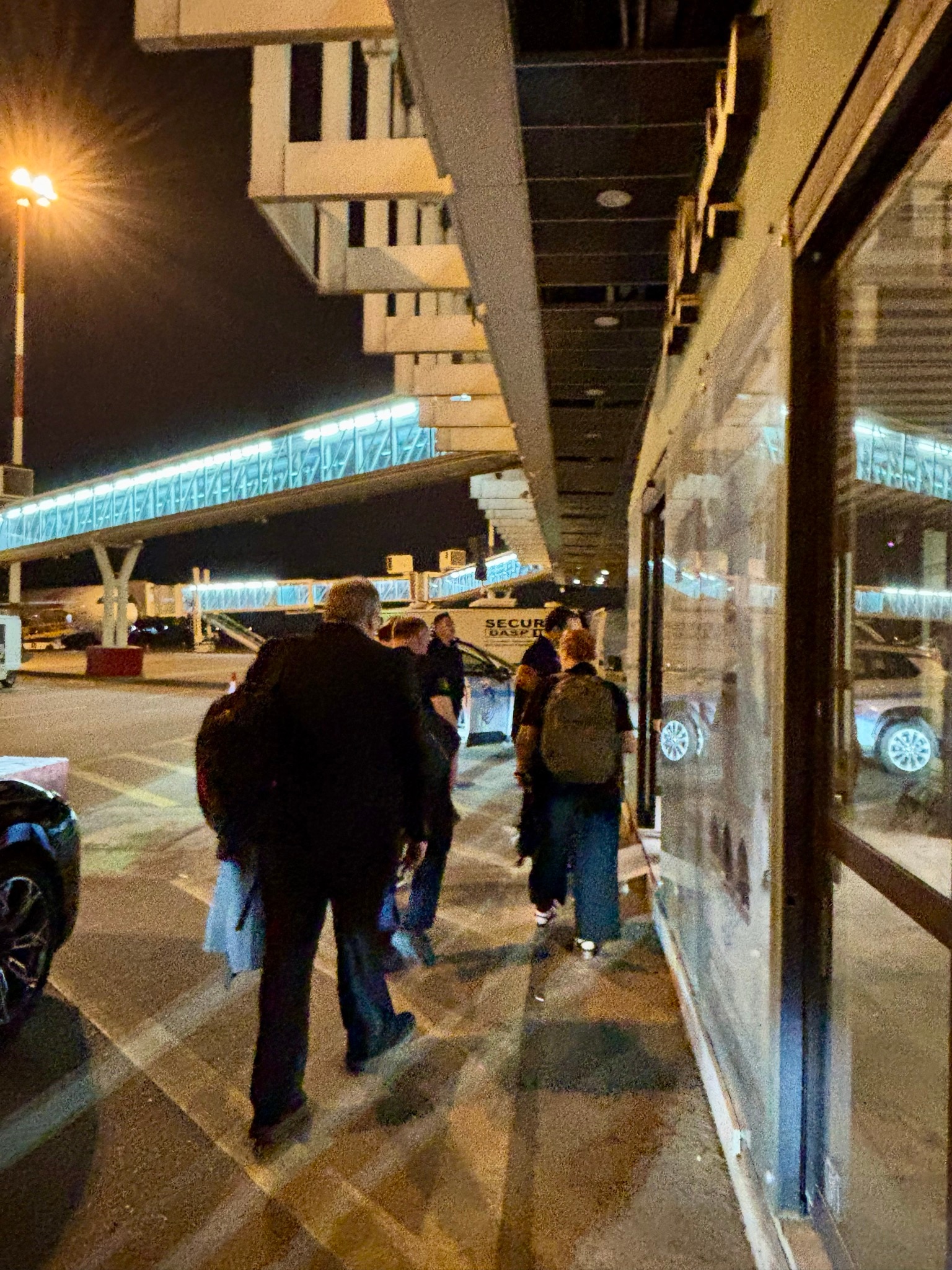 People pictured from behind walking at airport at night.
