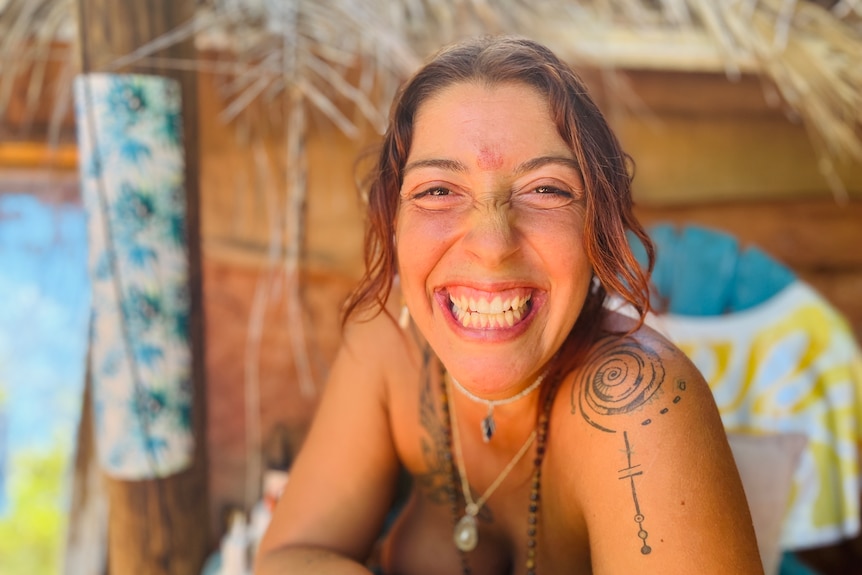 A woman with brown hair and tattoos smiles broadly