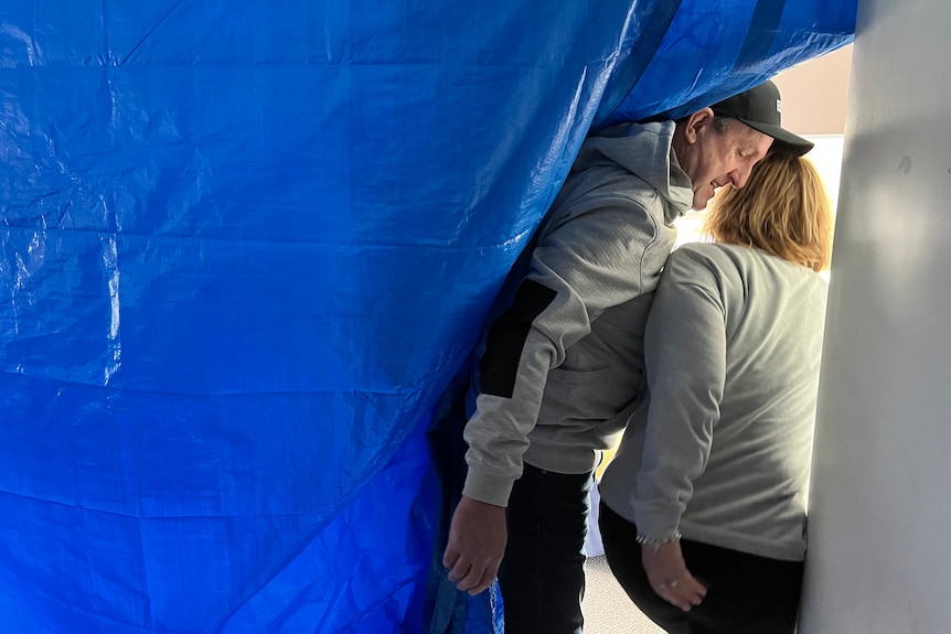 couple enter storm damaged home through blue tarp.