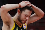 A male basketball player looks at the floor with his hands on his head.