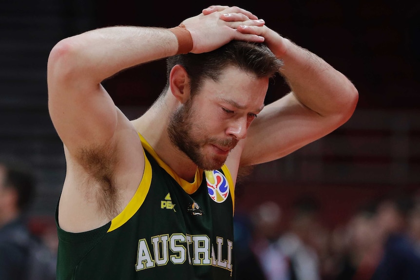 A male basketball player looks at the floor with his hands on his head.