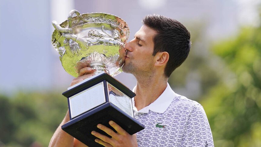 Novak Djokovic poses with a trophy in a park