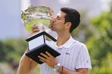 Novak Djokovic poses with a trophy in a park