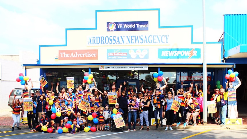 A large group of people wearing Adelaide Crows colours, gathered outside the Ardrossan Newsagency