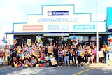 A large group of people wearing Adelaide Crows colours, gathered outside the Ardrossan Newsagency