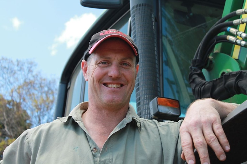 A man wearing a cap and a light green shirt leaning against a tractor.
