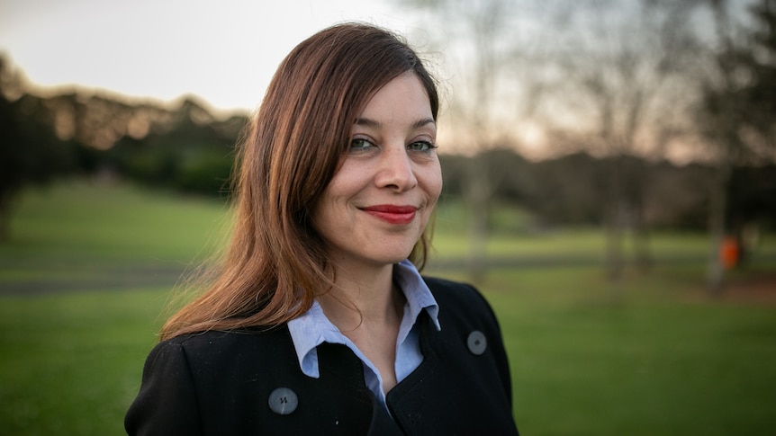 A woman with brown hair smiling in a park