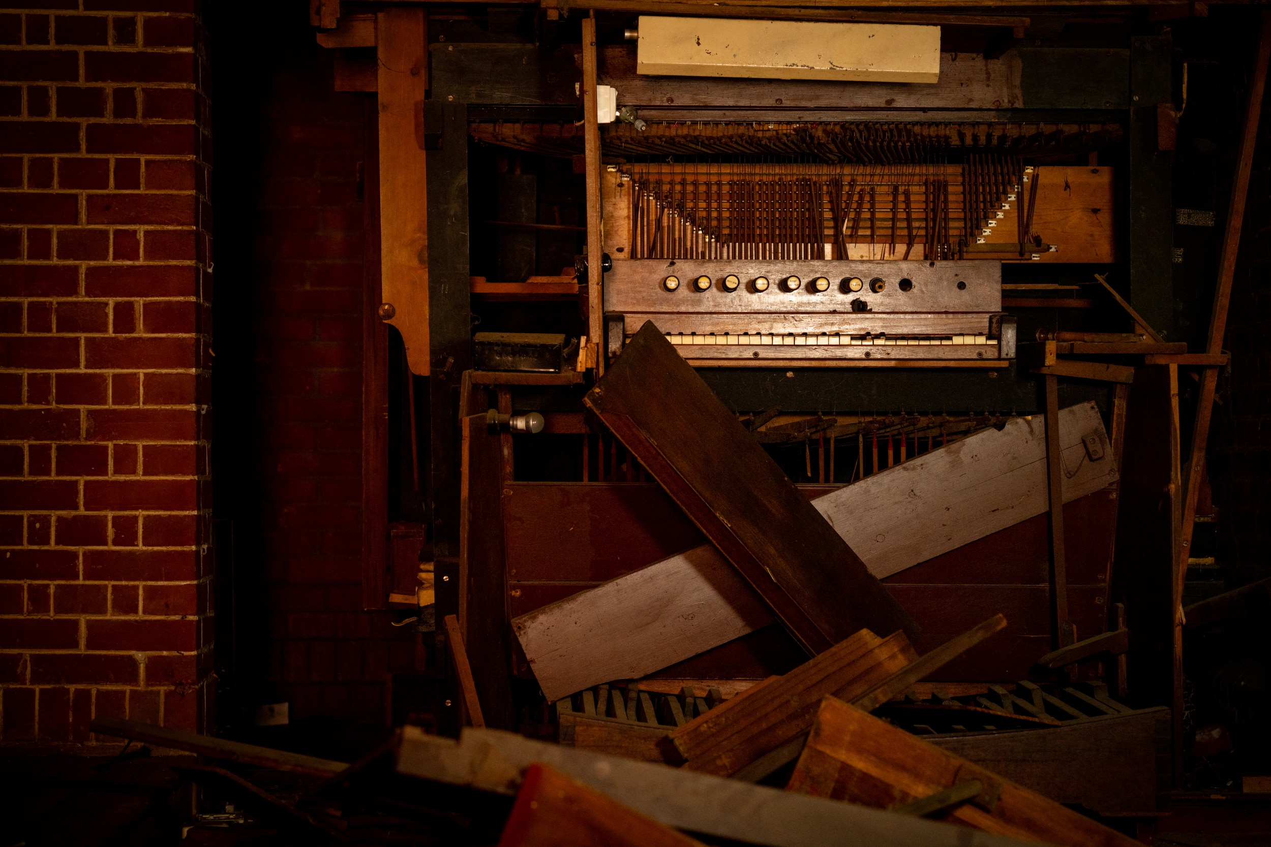 A dark coloured wooden organ instrument is damaged, with wood strewn on the ground