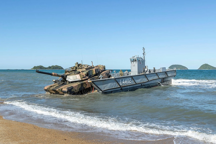 An army tank drives onto a beach after being unloaded from a navy landing craft during a military exercise