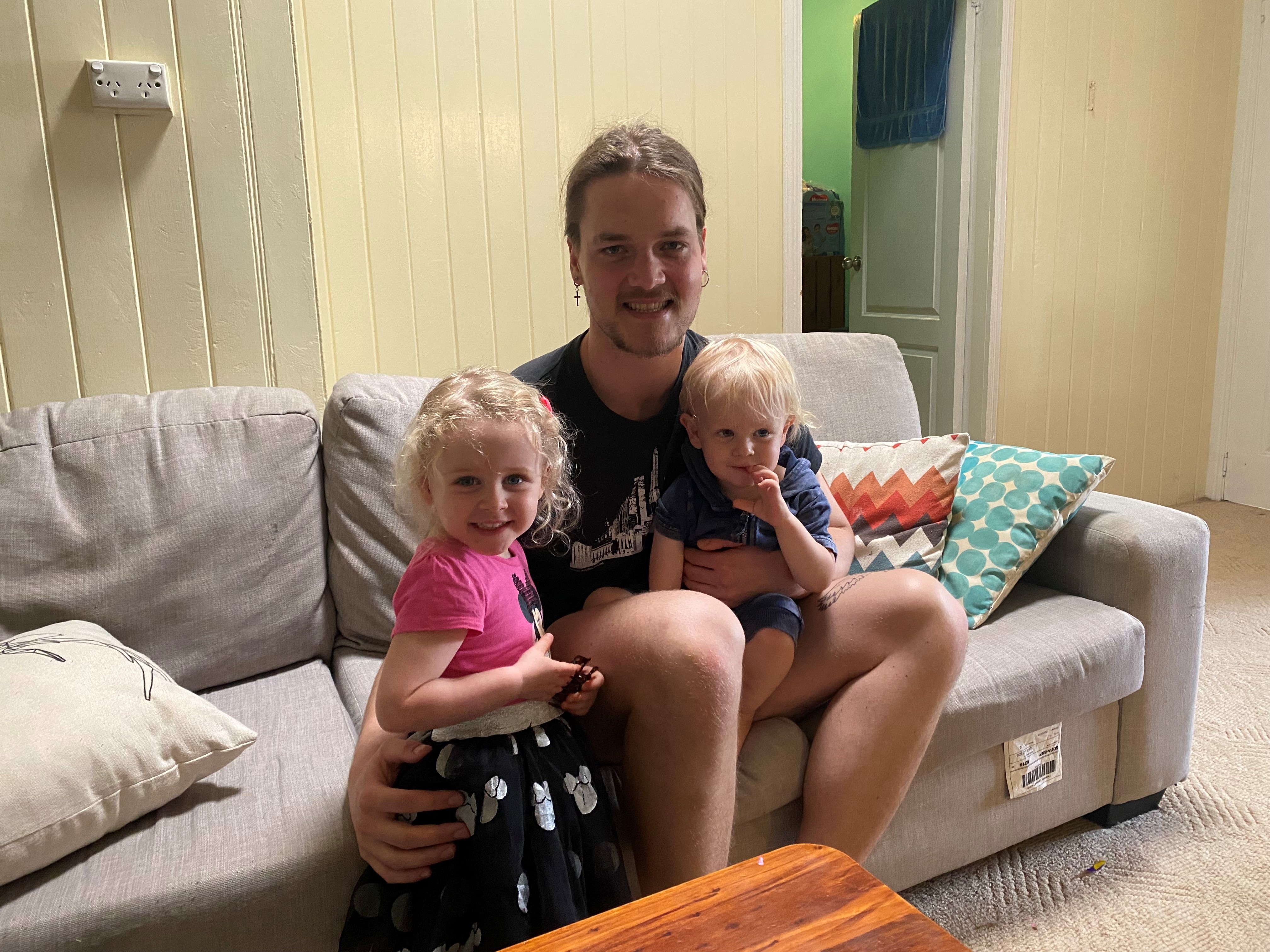 A young man sitting on a couch with two small children on his lap.