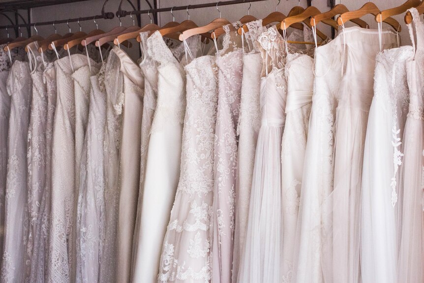 A row of white wedding dresses hanging on a rack.