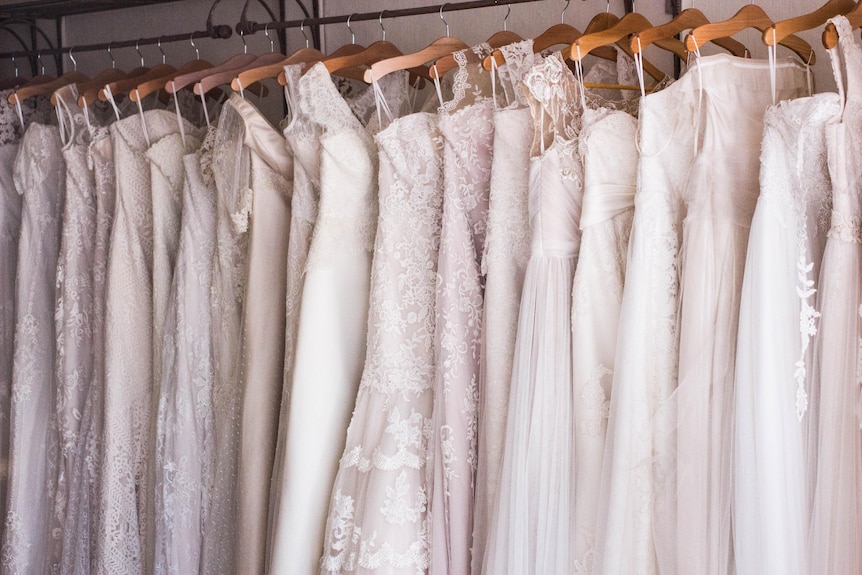 A row of white wedding dresses hanging on a rack.