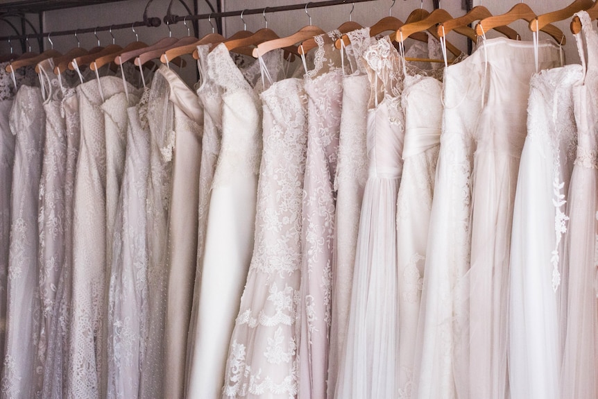 Dozens of wedding dresses hang on wooden clothing racks.