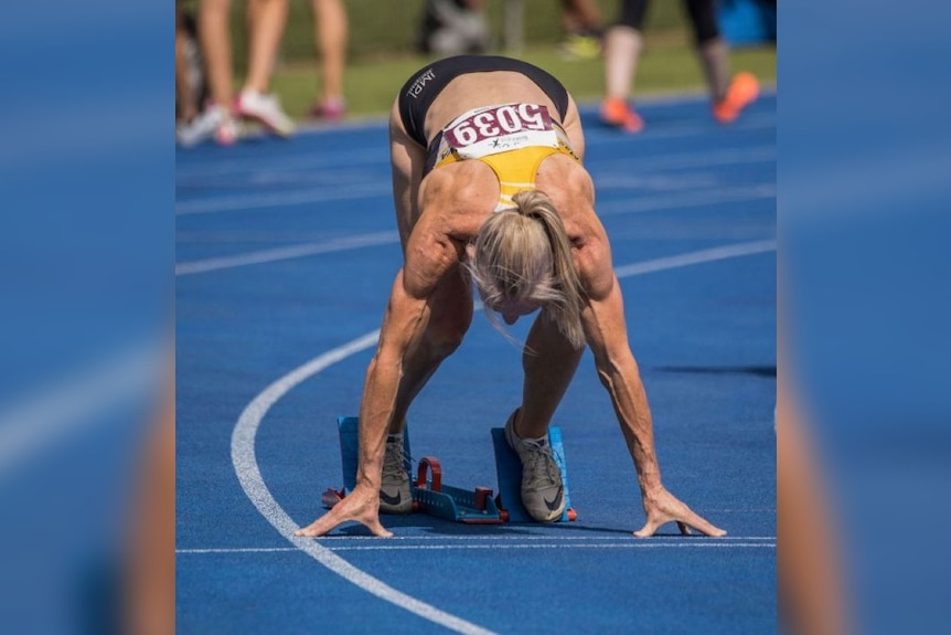 A woman squats down at the start of a running race.