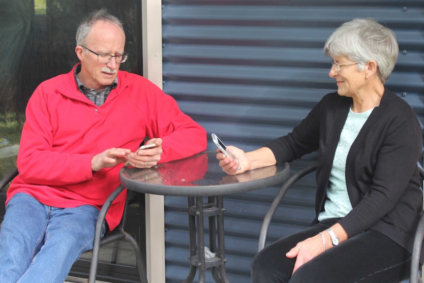 Karen and Stephen sitting at a table in front of their guesthouse, comparing reception on their phones.