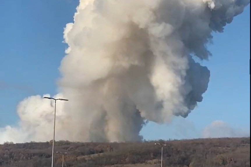 White smoke billows from a barren landscape containing buildings