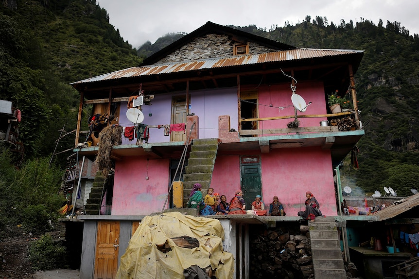 Women sit outside a rundown looking pink house in the Himalayas. 