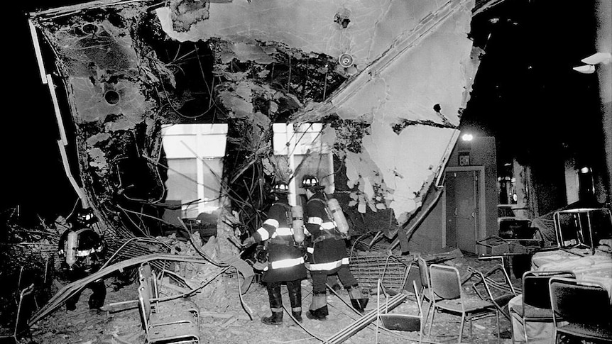 black and white image showing destruction inside world trade centre and firemen in front of the damage