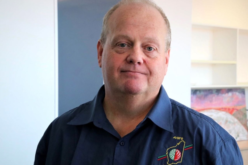 Mr Brown stands in an office looking at the camera. He wears a volunteer brigade shirt.