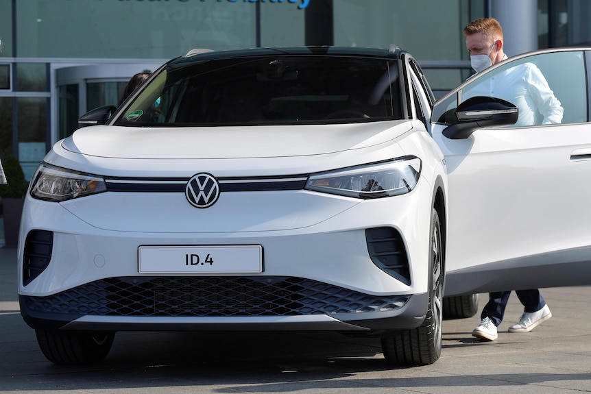 A man wearing a face mask gets into the drivers seat of a new white Volkswagen SUV.