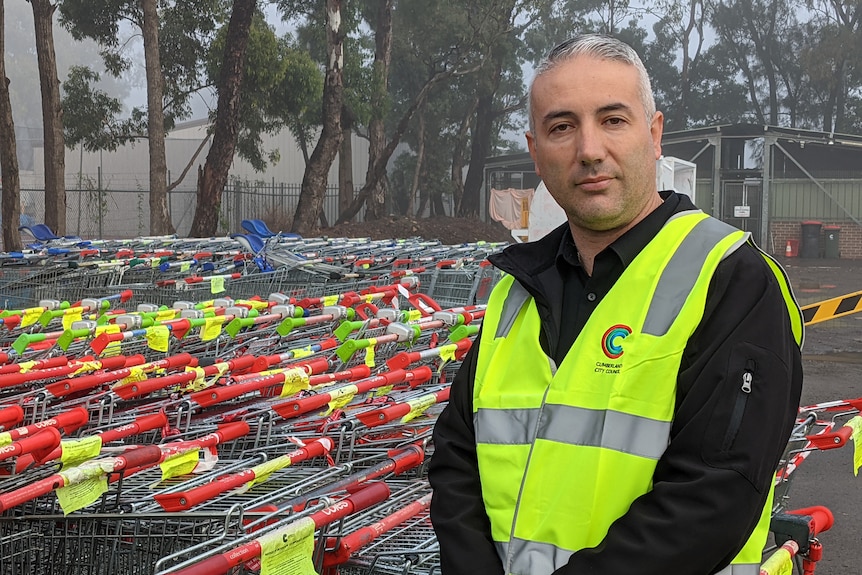 Steve Christou wears a high-vis vest while standing next to some shopping trolleys