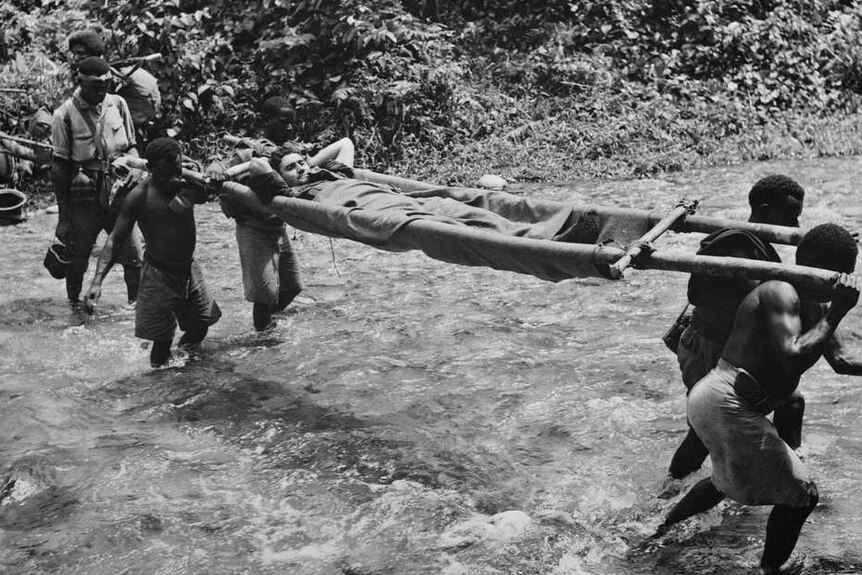 You see a black and white photo with Papua New Guinean men carrying a wounded allied soldier across a fast river.