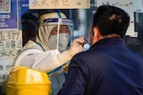 A medical worker in a protective suit collects a swab sample from a man in China.