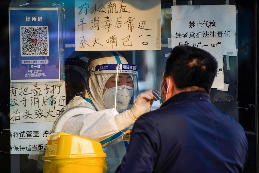 A medical worker in a protective suit collects a swab sample from a man in China.