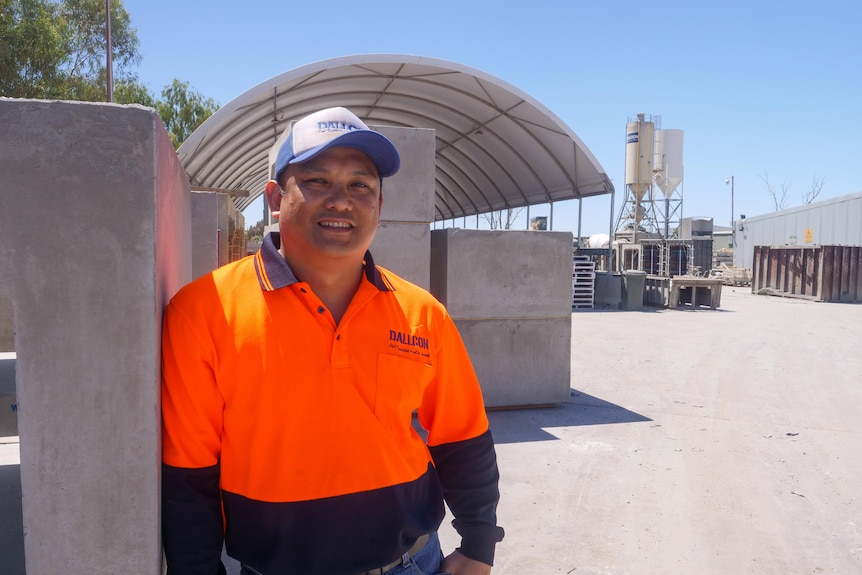 A Filipino man in a high vis orange shirt standing beside industrial concrete structures.