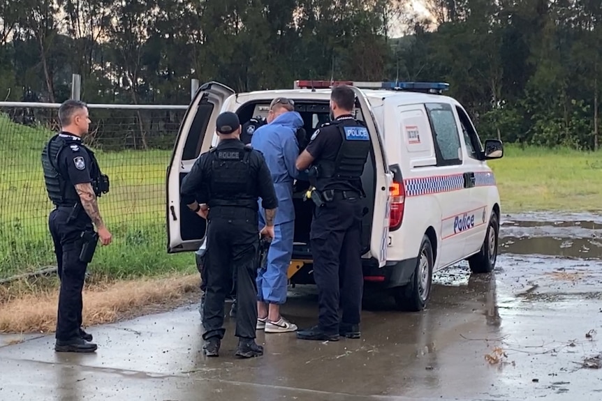 Officers arrest a man dressed in a forensic suit at the back of a marked police car.