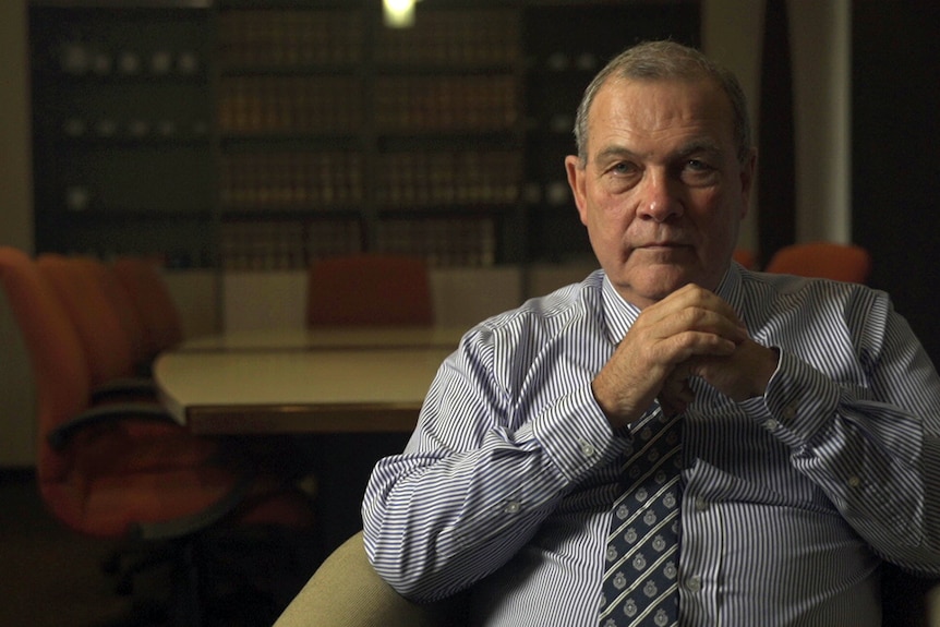 A portrait of a male lawyer sitting in a boardroom, serious expression