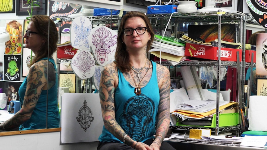 A woman with tattoos in a workspace at a tattoo parlour.