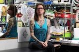 A woman with tattoos in a workspace at a tattoo parlour.