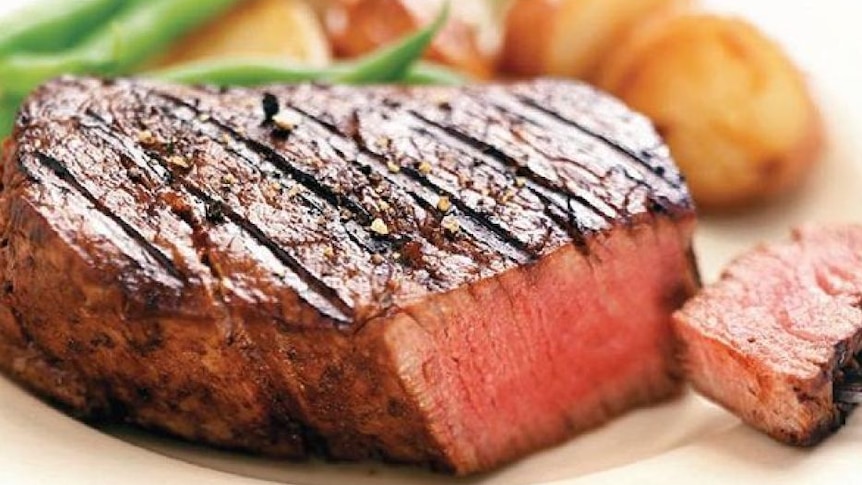 a hick medium rare cooked steak on a plate with vegetables in the background