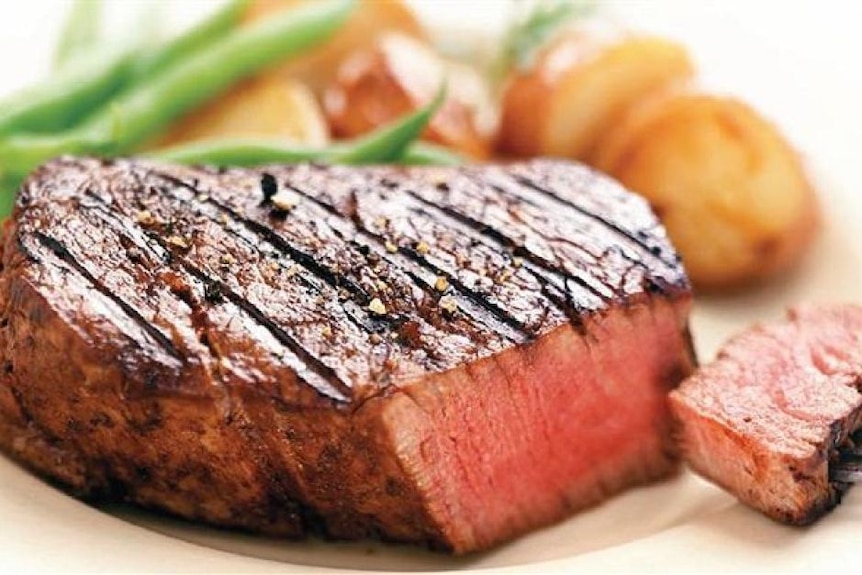 a hick medium rare cooked steak on a plate with vegetables in the background