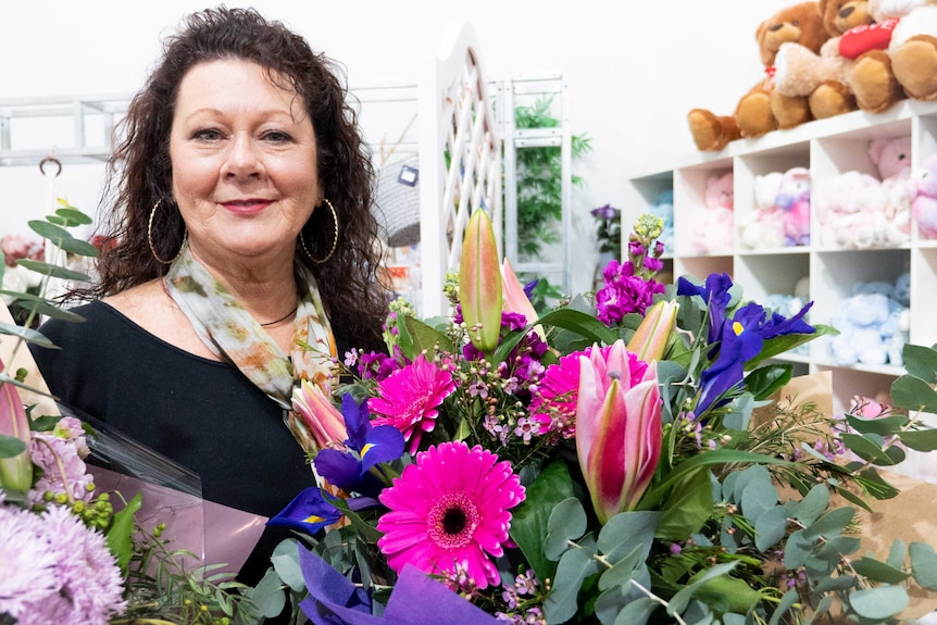 A woman holding a bunch of bright flowers standing in a florist.