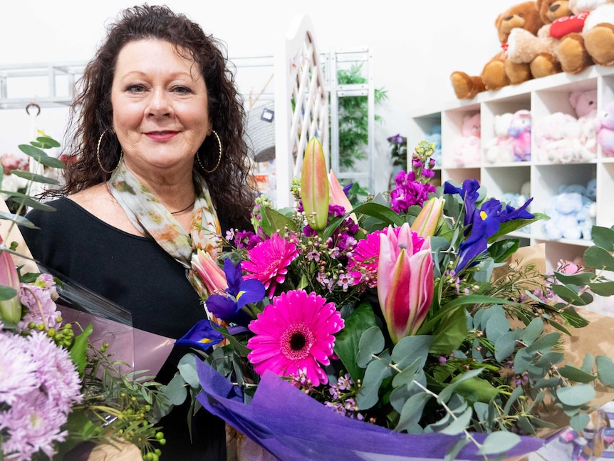 A woman holding a bunch of bright flowers standing in a florist.